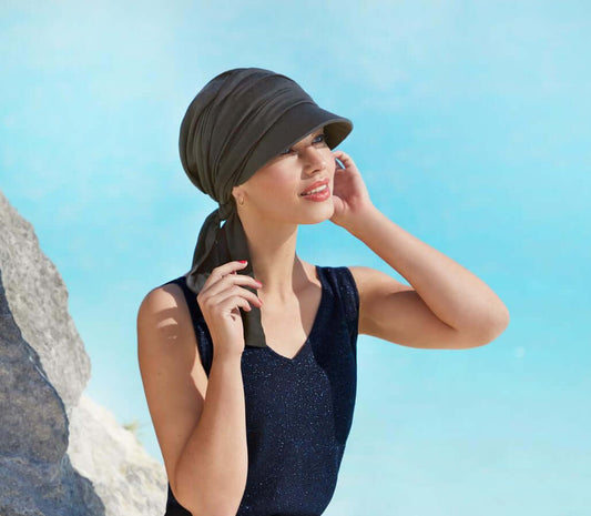 House of Christine B.B. Briana cap in Steel Grey worn by a woman near water, showcasing sun protection and summer style.