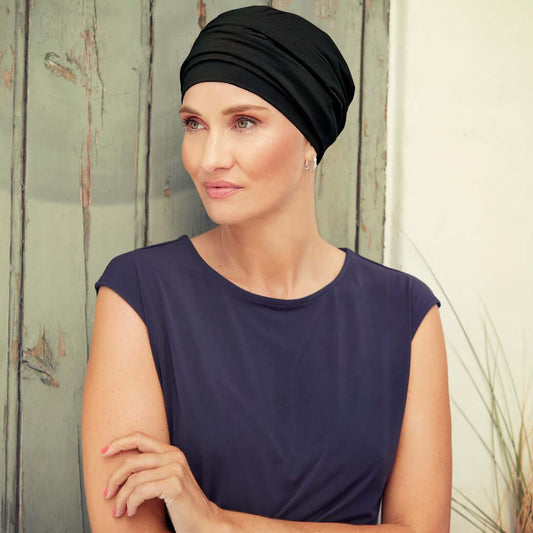 Model wearing a black HocNomi Turban, showcasing its classic design against a wooden background.